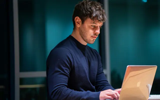 Man leest aandachtig informatie aan een tafel op zijn laptop.