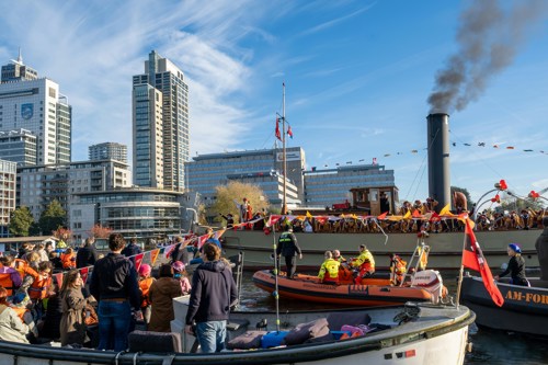 Gezinnen met kinderen kijken naar de Sinterklaasintocht waar ook een reddingsbrigade boot te zien is.